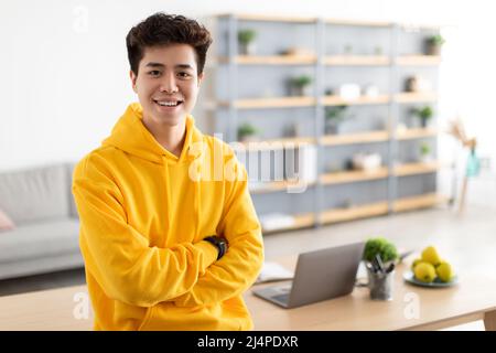 Bedingt lächelnder asiatischer Mann, der mit gefalteten Armen posiert Stockfoto