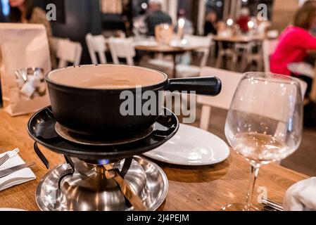 Beheizter Topf mit schweizer Käsefondue neben Weinglas auf dem Esstisch Stockfoto