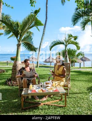 Frühstück an einem Strand mit Palmen und einem Pool in Mauritius, tropischer Rahmen mit Frühstück.Paar Mann und Frau frühstücken im tropischen Garten Stockfoto