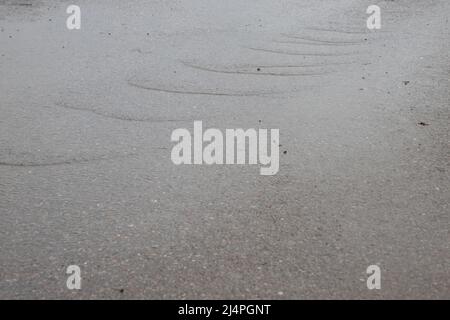 Nach dem Regen fließt Wasser einen Gehweg hinunter, um den Hintergrund zu sehen Stockfoto