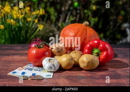 Verschiedene Gemüsesorten auf einem Holztisch sowie europäische Banknoten und Münzen, die die Inflation symbolisieren. Stockfoto