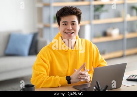 Am Schreibtisch sitzender, zustandig lächelnder asiatischer Mann, der posiert Stockfoto