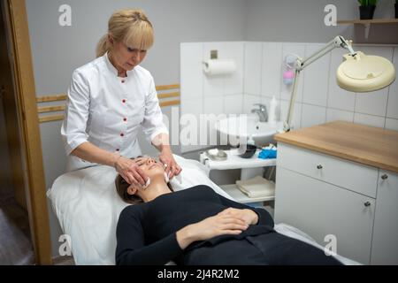 Der Arzt von Beutician wischt das Gesicht des Patienten mit Wattebäcken ab. Portrait der Frau über Reinigung Gesicht Verfahren von Frau Kosmetologin in der Beauty-Klinik. Schönheit Stockfoto