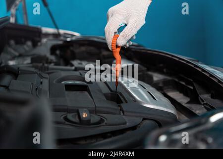 Nahaufnahme einer Handschaufel, die einen Ölmessstab aus dem Motor zieht. Das Konzept der Autoreparatur in einer Autowerkstatt. Stockfoto