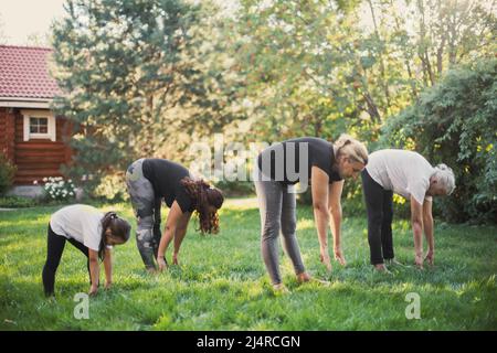 Eine Familie einige Generationen Sport zusammen auf dem Hinterhof versuchen, Boden mit Händen in der gleichen Weise stehen auf Wiese voll von grünem Gras und zu berühren Stockfoto