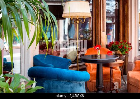tulpe in Glas auf Tisch Street Cafe Terrasse mit weichen farbigen Sesseln auf Holzboden am Fenster mit Eingangstür und Blumen mit dekorativen fl Stockfoto