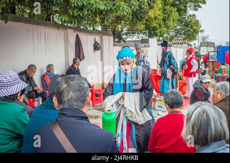 ANQING, CHINA - 23. März: Straßenkünstler führen am 23. März 2014 eine traditionelle Oper auf der Straße auf. Eine Schauspielerin serviert heißes Trinkwasser zum Zuschauen Stockfoto