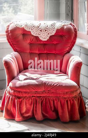Vintage-Schaukelstuhl mit getufteten, staubigen rosafarbenen Samten und Rüschen in der Ecke des Zimmers. Stockfoto