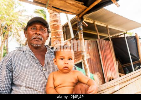 Ein reifer Mann, ein armer Fischer aus Lateinamerika, trägt seine Tochter auf den Beinen in einer ländlichen Gemeinde in Leon, Nicaragua Stockfoto