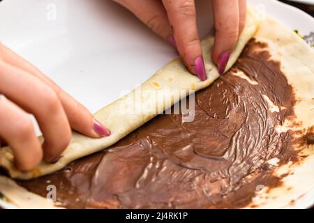 Zubereitung und Rollen leckere Crepes oder Pfannkuchen mit Schokoladencreme, Nahaufnahme. Süßes hausgemachtes Dessert Stockfoto