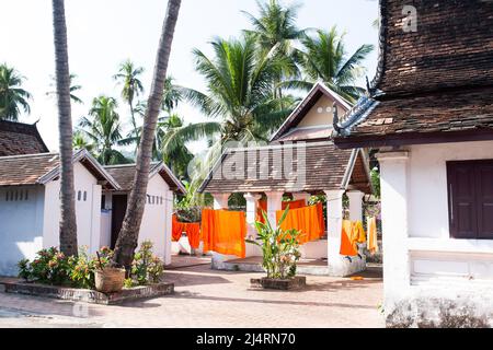 Monastische Roben, Safranroben, die im Sonnenlicht in einem alten Kloster in Luang Prabang, Laos, an der Wäscheleine hängen. Stockfoto