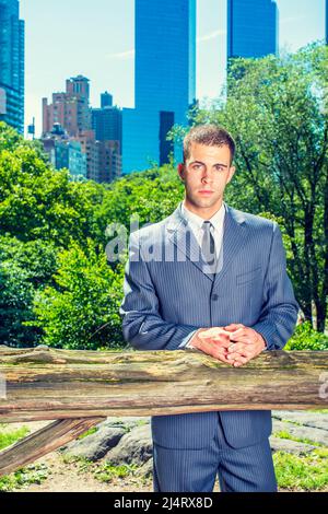 Junger Geschäftsmann wartet draußen. Formell in einem blauen Anzug, schwarzer Krawatte, ein junger professioneller Kerl steht in einem Waldgebiet in der Nähe einer Business DIS Stockfoto