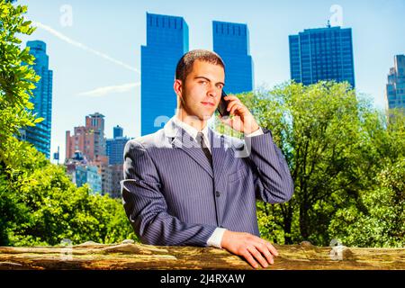 Junger Geschäftsmann am Telefon. Ein junger Student, der sich formell in einem blauen Anzug, einer schwarzen Krawatte, kleidet, steht vor dem Geschäftsviertel, ma Stockfoto