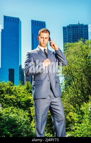 Junger Geschäftsmann am Telefon. Formell in einem blauen Anzug, schwarzer Krawatte, ein junger Profi steht vor dem Geschäftsviertel, l Stockfoto