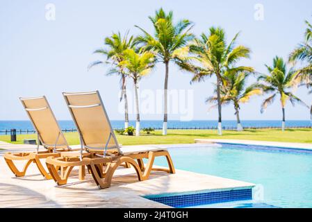 Poolbetten neben dem Swimmingpool mit Blick auf Kokospalmen und das Meer Stockfoto