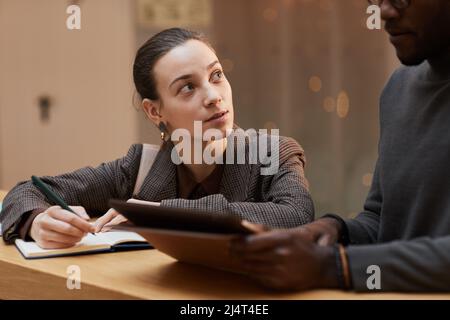 In warmen Farbtönen gehaltene Darstellung einer jungen Frau, die mit einem Kollegen an der Theke im Bürogebäude spricht Stockfoto