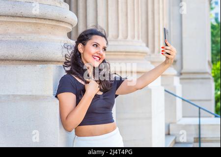 Schönes Mädchen machte Bilder von ihrem selbst. Ein junger, hübscher Student streckt sich den Arm, hält ein mobiles Gerät und schaut draußen durch eine Kamera Stockfoto