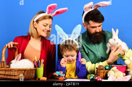 Traditionen der Osterfamilie. Glückliche Mutter, Vater und kleiner Sohn in Hasenohren, die sich auf den Urlaub vorbereiten. Stockfoto