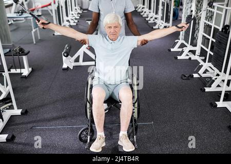 Porträt eines älteren Mannes im Rollstuhl, der im Fitnessstudio in der Gesundheitsklinik körperliche Übungen macht Stockfoto