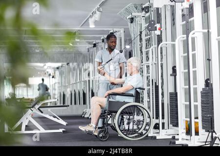 Seitenansicht Porträt eines älteren Mannes im Rollstuhl, der Übungen im Fitnessstudio in der Rehabilitationsklinik macht, Kopierraum Stockfoto