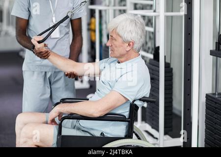 Seitenansicht Porträt eines älteren Mannes im Rollstuhl, der Rehabilitationsübungen im Fitnessstudio in der Klinik macht, Kopierraum Stockfoto