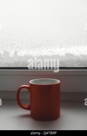 Kaffeetasse auf einem regnerischen Tag Fenster Hintergrund. Selektiver Fokus. Wassertropfen Hintergrund. Stockfoto
