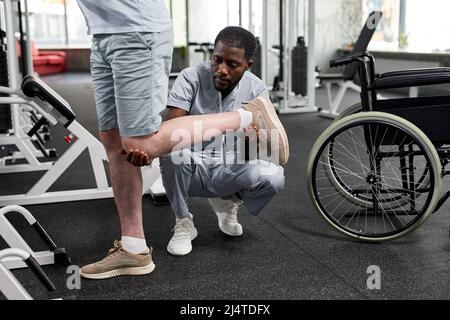 Porträt eines afroamerikanischen Rehabilitationstherapeuten, der Patienten bei der Durchführung von Mobilitätsübungen im Fitnessstudio und im Kopierraum unterstützt Stockfoto