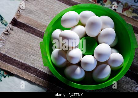 Verschiedene weiße Eier, gruppiert in einer grünen Schüssel auf dem Tisch und weiche Seitenbeleuchtung Stockfoto