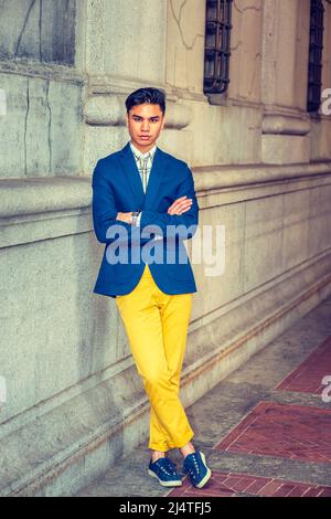 Mann, Der Sich Draußen Entspannt. In blauen Blazer, gelbe Hosen, Sneakers, Armbanduhr, ein junger gutaussehender Kerl steht an der Wand im alten Mode-Stil, crossin Stockfoto