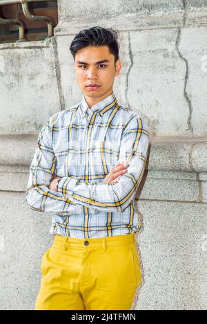 Porträt des Stadtjungen. In gelb-weißen, gemusterten Hemden, gelben Hosen, überkreuzten Armen, steht ein junger, gutaussehender Kerl im alten Mode-Stil Stockfoto