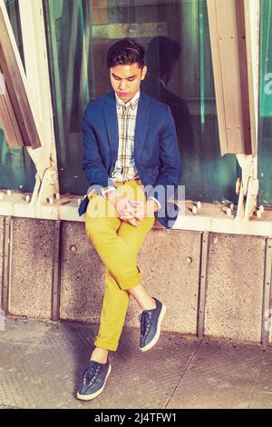 Einsamer Mann. Dressing in blauen Blazer, gemustert unter Verschleiß, gelbe Hosen, Turnschuhe, Hände kreuzen, Beine, sengenden Kopf, ein junger, hübscher Kerl ist Sitti Stockfoto