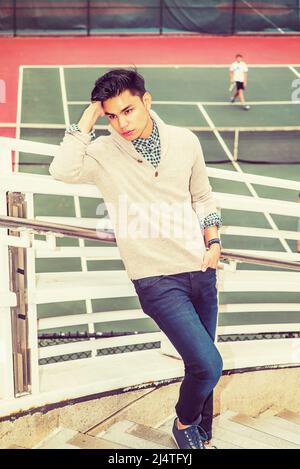 Einsamer Mann. Dressing in hellgrau gekleiden Pullover mit Schalkragen Cardigan, blaue Jeans, Hand stützenden Kopf, Arm auf Geländer ruhen. Ein junger Kerl ist Stockfoto