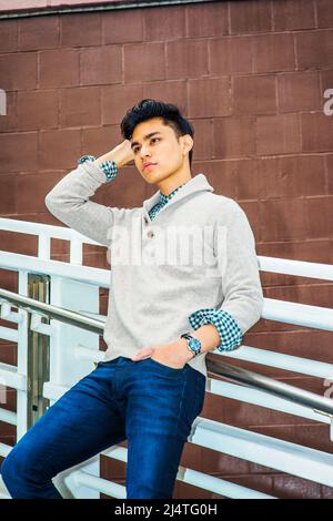 Mann, Miss Dich. In hellgrauem, gekleidtem Pullover mit Schalkragen, Cardigan, blauer Jeans, einem kratzenden Kopf der Hand, einer Hand in der Tasche, ist ein junger Mann s Stockfoto