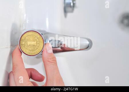 Wasserhähne im Badezimmer mit einer ukrainischen Griwna-Münze, Übersetzung aus dem Ukrainischen: Eine Griwna, ukraine. Stockfoto