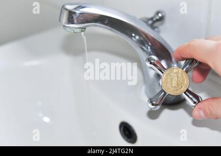 Wasserhähne im Badezimmer mit einer ukrainischen Griwna-Münze, Übersetzung aus dem Ukrainischen: Eine Griwna, ukraine. Stockfoto