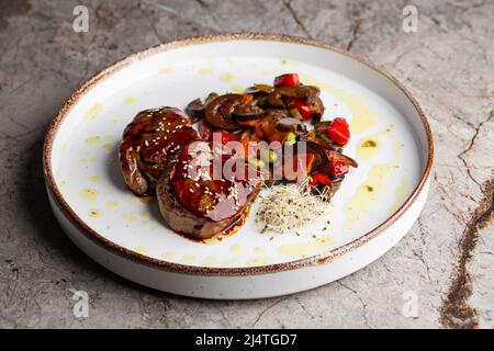 Gegrilltes Fleisch-Filetsteak in Speckmedaillons mit Himbeersoße eingewickelt, serviert mit Gemüse und Pilzen Stockfoto