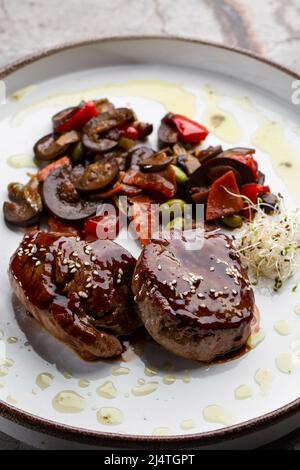 Gegrilltes Fleisch-Filetsteak in Speckmedaillons mit Himbeersoße eingewickelt, serviert mit Gemüse und Pilzen Stockfoto