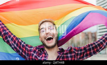 Schwuler Mann mit Make-up auf winkender Regenbogenflagge im Freien - LGBTQ Drag Queen Konzept Stockfoto