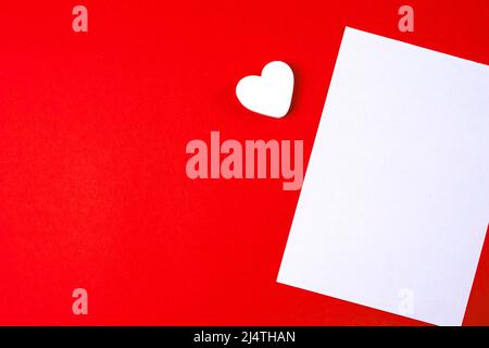 Vorlage zum Nachbau des Liebesbriefes. Leeres, weißes Papier auf rotem Papierhintergrund und ein weißes Herz mit Kopierraum. Stockfoto