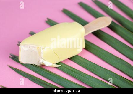 Vanilleeis auf Stick mit weißer Schokolade auf rosa Hintergrund mit einem Palmblatt überzogen. Sommerkonzept. Stockfoto