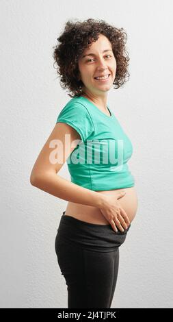 Eine friedliche, schwanger kaukasische Frau umarmte ihren Bauch vor einem isolierten weißen Hintergrund Stockfoto