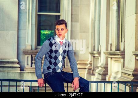 Mann, Der Sich Draußen Entspannt. In einem schwarz-weißen, grau gemusterten Pullover, Jeans, sitzt ein junger, gutaussehender Profi auf einem Geländer in einem Büro BU Stockfoto