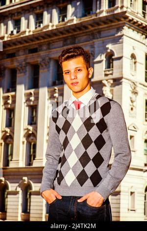 Porträt eines Studenten. Kleid in einem schwarzen, weißen, grau gemusterten Pullover, Jeans, Hände in Taschen, Ein junger, gutaussehender Geschäftsmann steht da Stockfoto