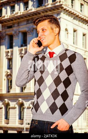 Mann, Der Nach Draußen Ruft. In einem schwarz-weißen, grau gemusterten Pullover, Jeans, steht ein junger, gutaussehender Geschäftsmann vor einem Bürogebäude Stockfoto