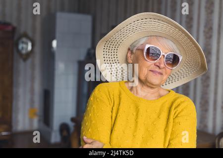 Fühlt sich an wie Sommer. Nette ältere Frau in Hut und Sonnenbrille zu Hause Medium closeup Wohnzimmer Dienstalter Konzept. Hochwertige Fotos Stockfoto