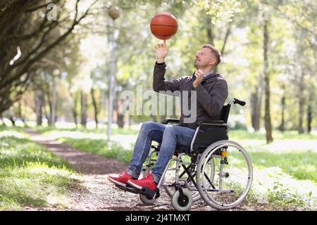 Mann dreht Basketball, während er im Rollstuhl im Park sitzt Stockfoto