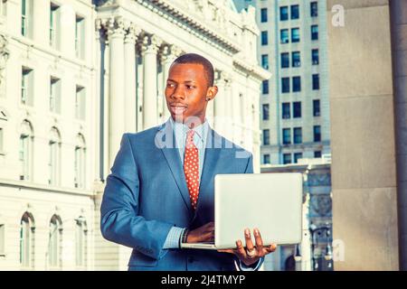 Geschäftsmann, der auf der Straße arbeitet. Formell in blauem Anzug, gemustertem Unterhemd, Krawatte, kurzem Haarschnitt kleidet, steht ein junger Schwarzer in einem Business d Stockfoto