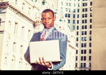 Geschäftsmann, der auf der Straße arbeitet. Formell in blauem Anzug, gemustertem Unterhemd, Krawatte, kurzem Haarschnitt kleidet, steht ein junger Mann in einem Business-Distric Stockfoto