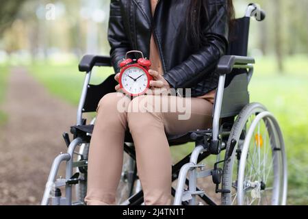 Frau im Rollstuhl hält Wecker im Park Stockfoto