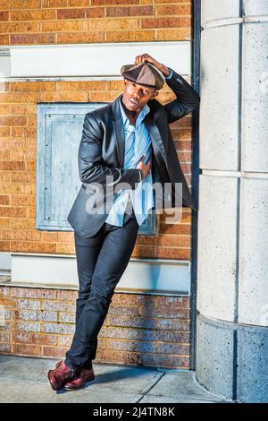 Man Urban Fashion. In modischer Newsboy-Mütze, schwarzem Blazer, Hosen und braunen Lederschuhen steht ein junger Schwarzer an der Ecke Stockfoto